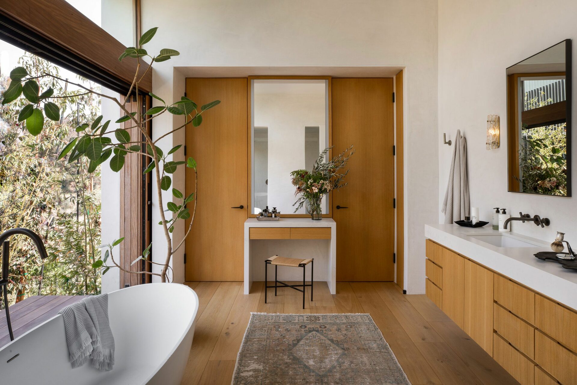 A bathroom with wooden flooring and a large window, providing ample natural light