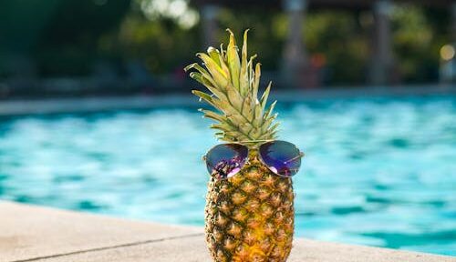 Free Tropical pineapple wearing sunglasses by a sunny swimming pool, perfect for vacation vibes. Stock Photo