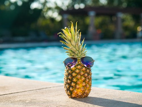 Free Tropical pineapple wearing sunglasses by a sunny swimming pool, perfect for vacation vibes. Stock Photo