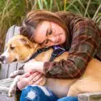 A young girl with epilepsy hugging a brown dog and wondering about how to get a free service dog for epilepsy