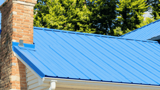 Blue metal roof with diagonal ridges, adjacent to a brick chimney. Evergreen trees in the background, conveying a bright, clear day.