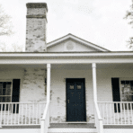 full house exterior with lime-washed white brick, weathered texture, moss streaks, front porch visible