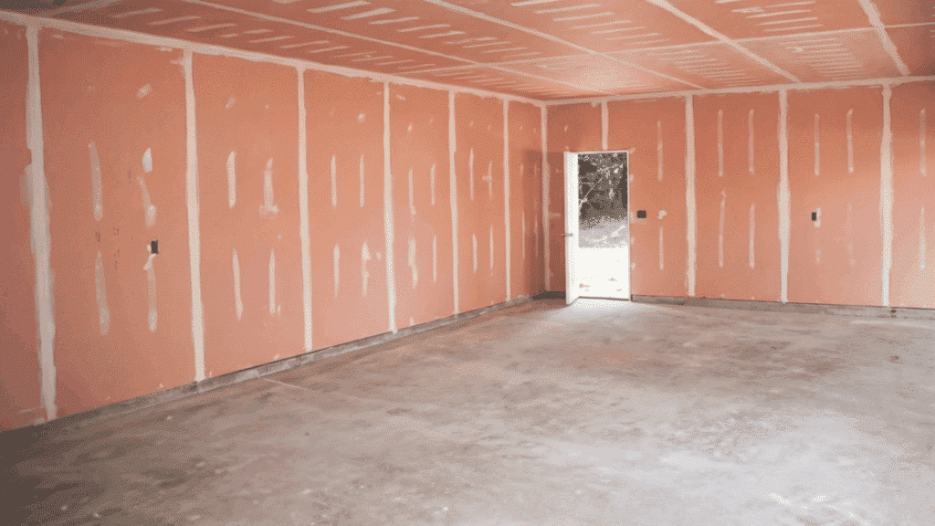 a room with pink fire-resistant drywall installed, showing seams and edges, ready for finishing and additional construction work