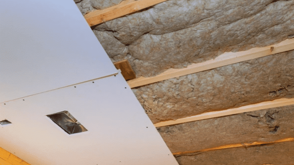soundproof drywall being installed on a ceiling with insulation visible between the beams