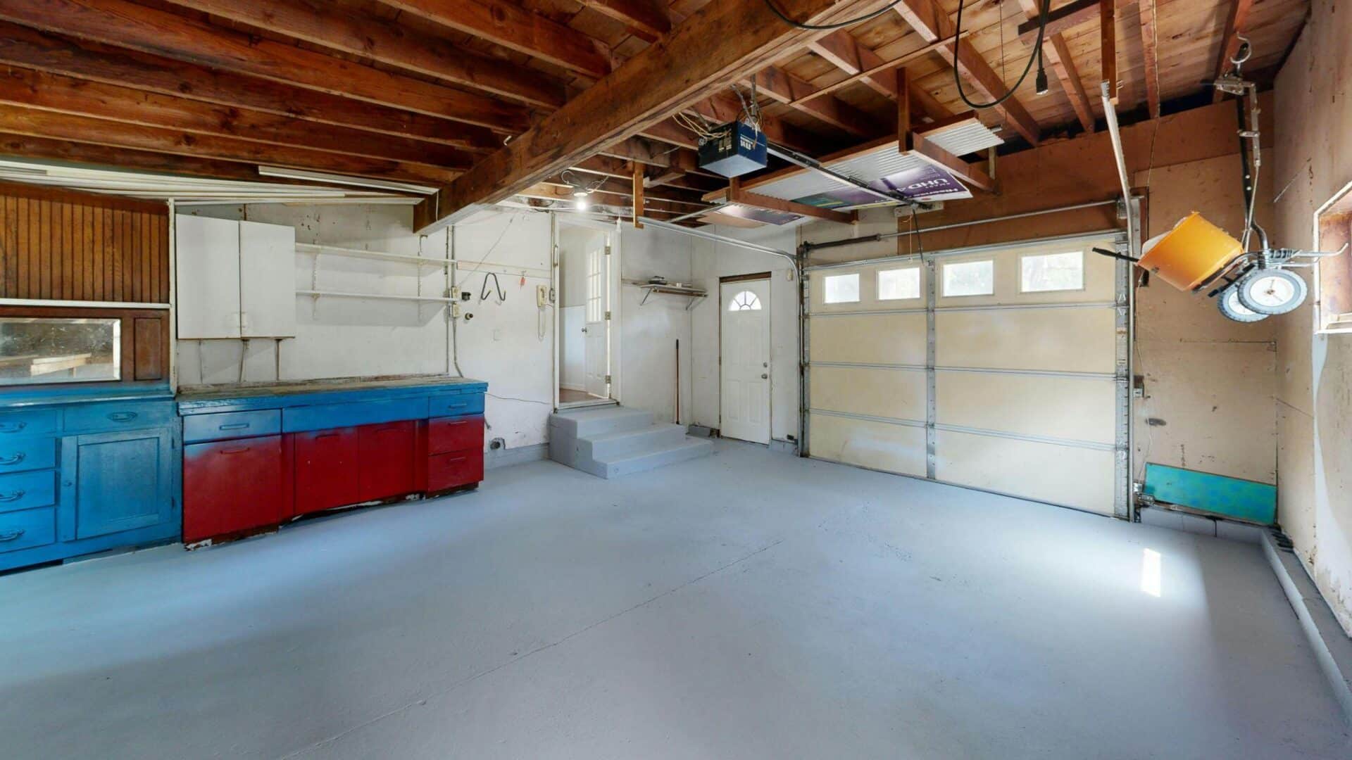Spacious garage with blue and red cabinets.